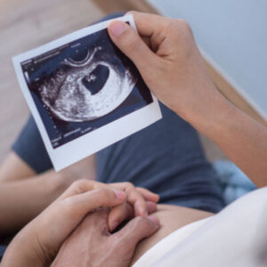 Hand of husband embraced the pregnant woman’s belly holding an u